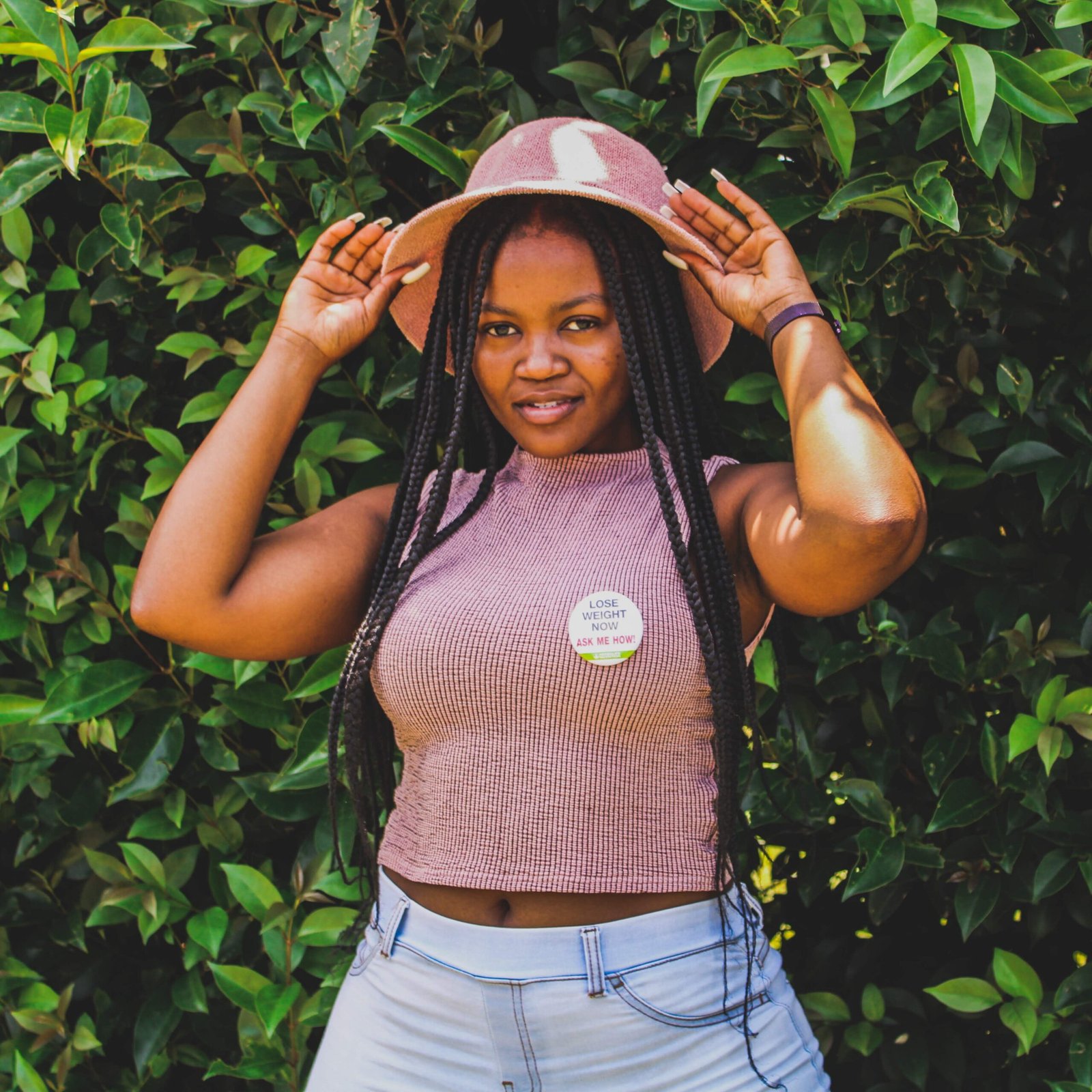 African woman in a stylish outfit poses in greenery with a hat in South Africa.