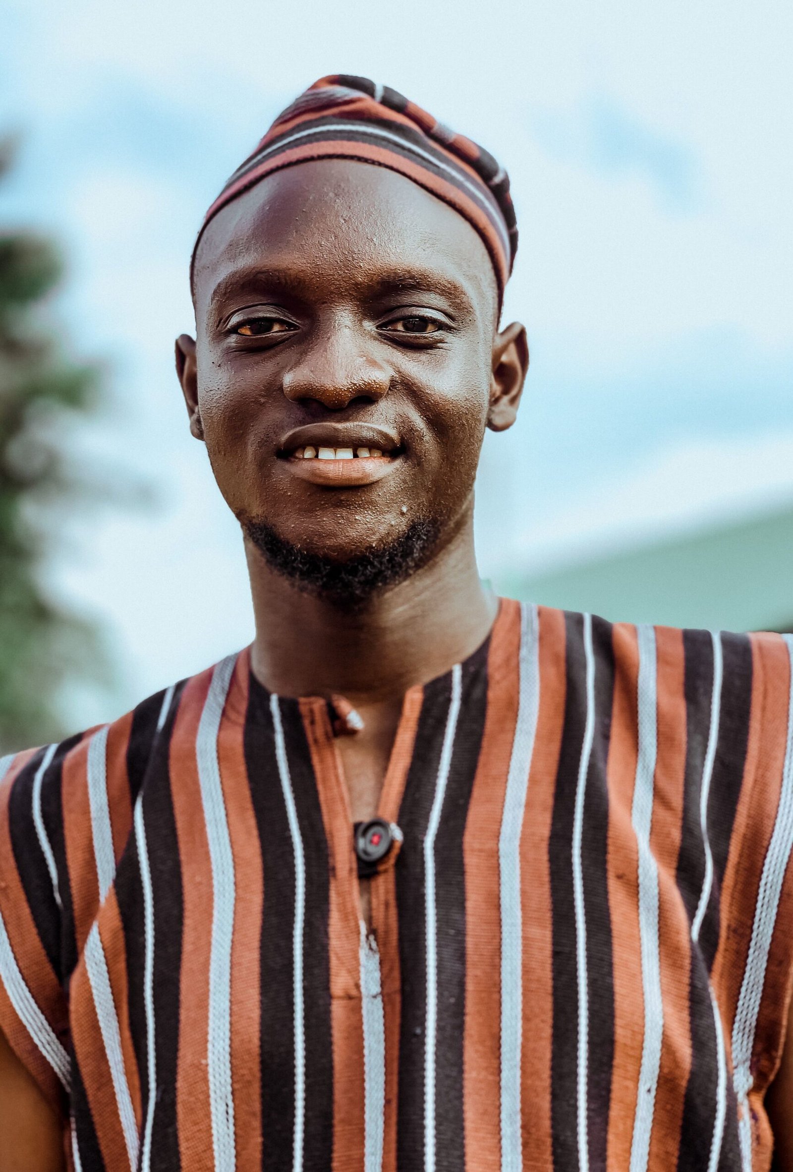 Portrait of a smiling African man wearing traditional attire, outdoors.