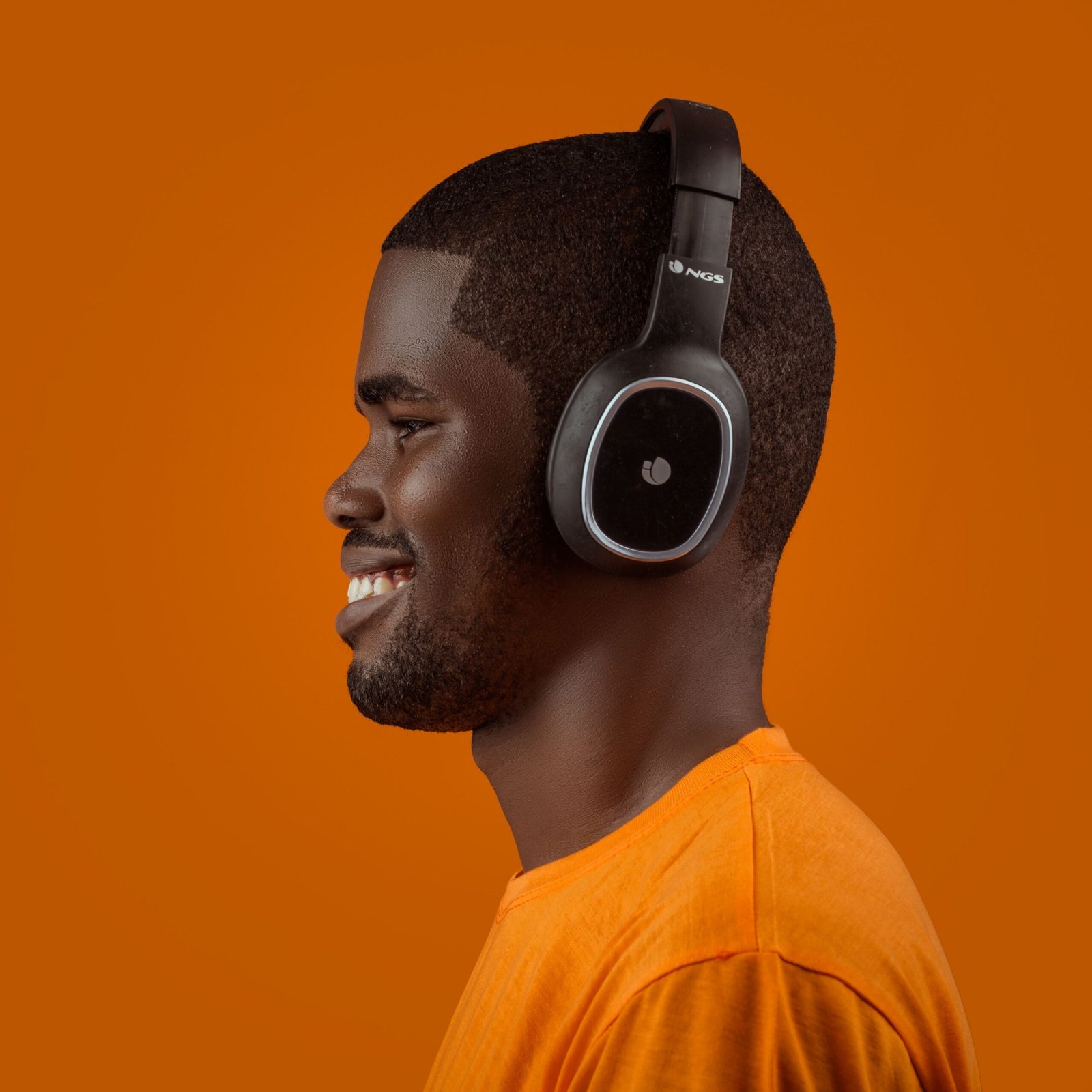 Profile of a smiling man wearing headphones against a vibrant orange background.