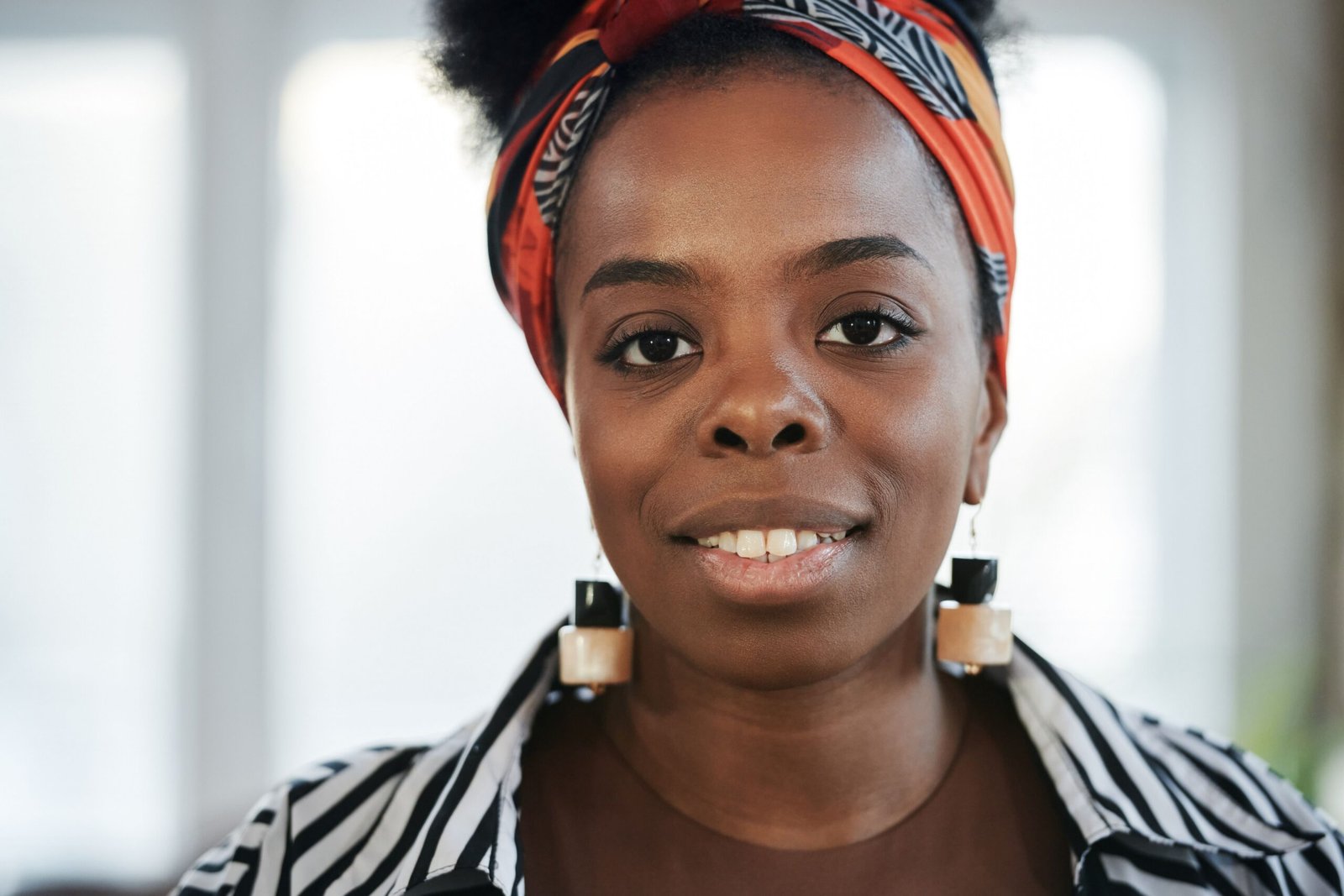 Close-up portrait of a smiling African American woman wearing a headscarf and earrings indoors.
