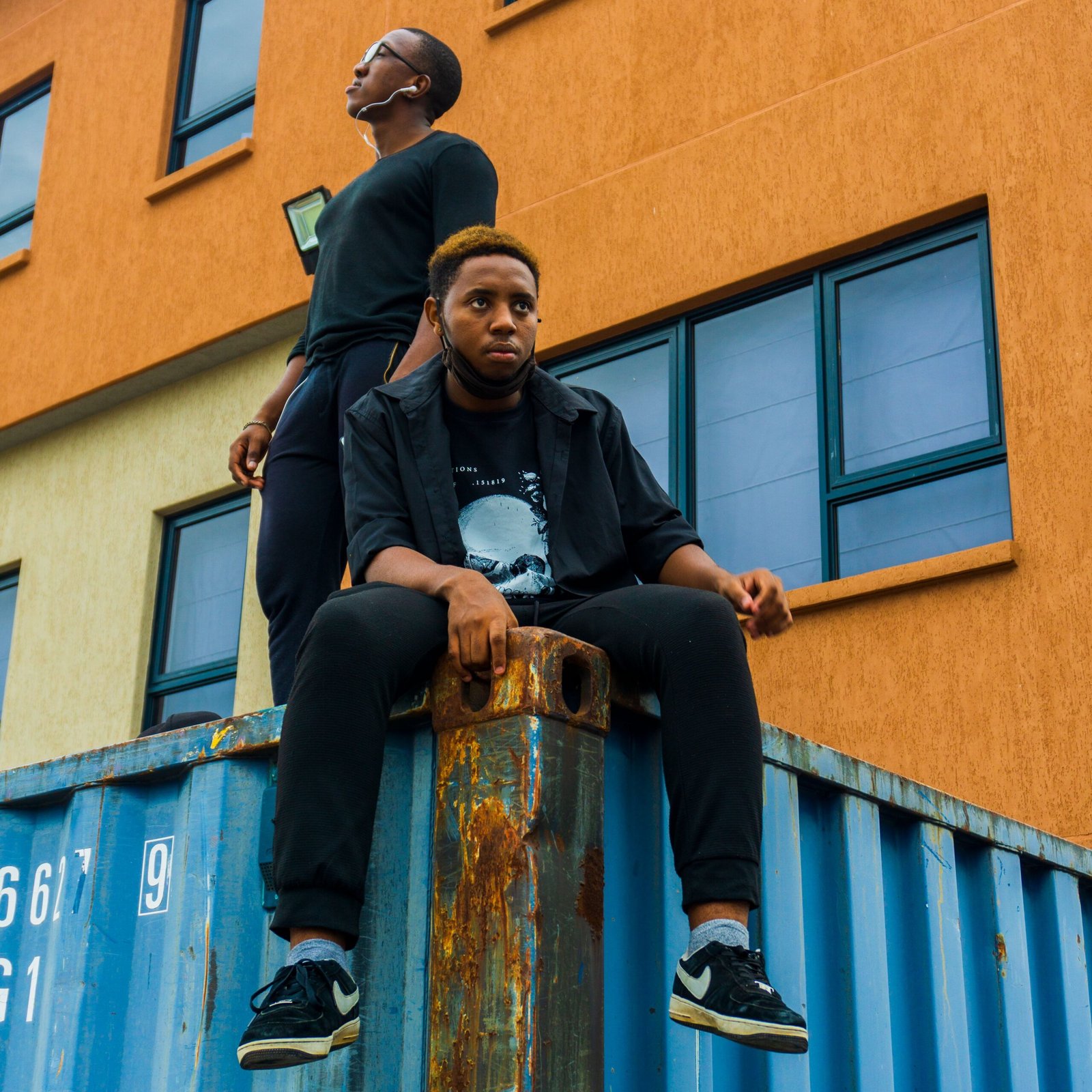 Stylish young men posing on a shipping container in city background, showcasing urban fashion.